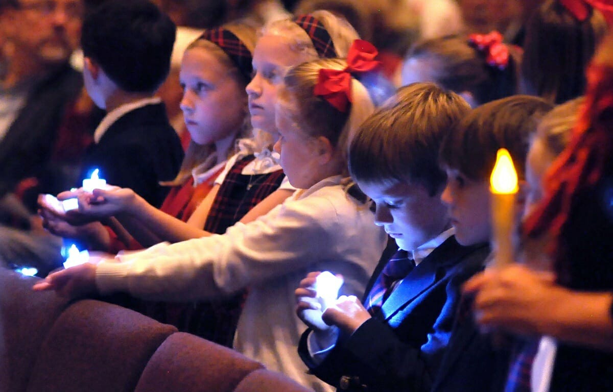 Caleb Baker, a first-grader at Holy Trinity school, gazes at his blue electronic candle while second-graders sing a Christmas carol.