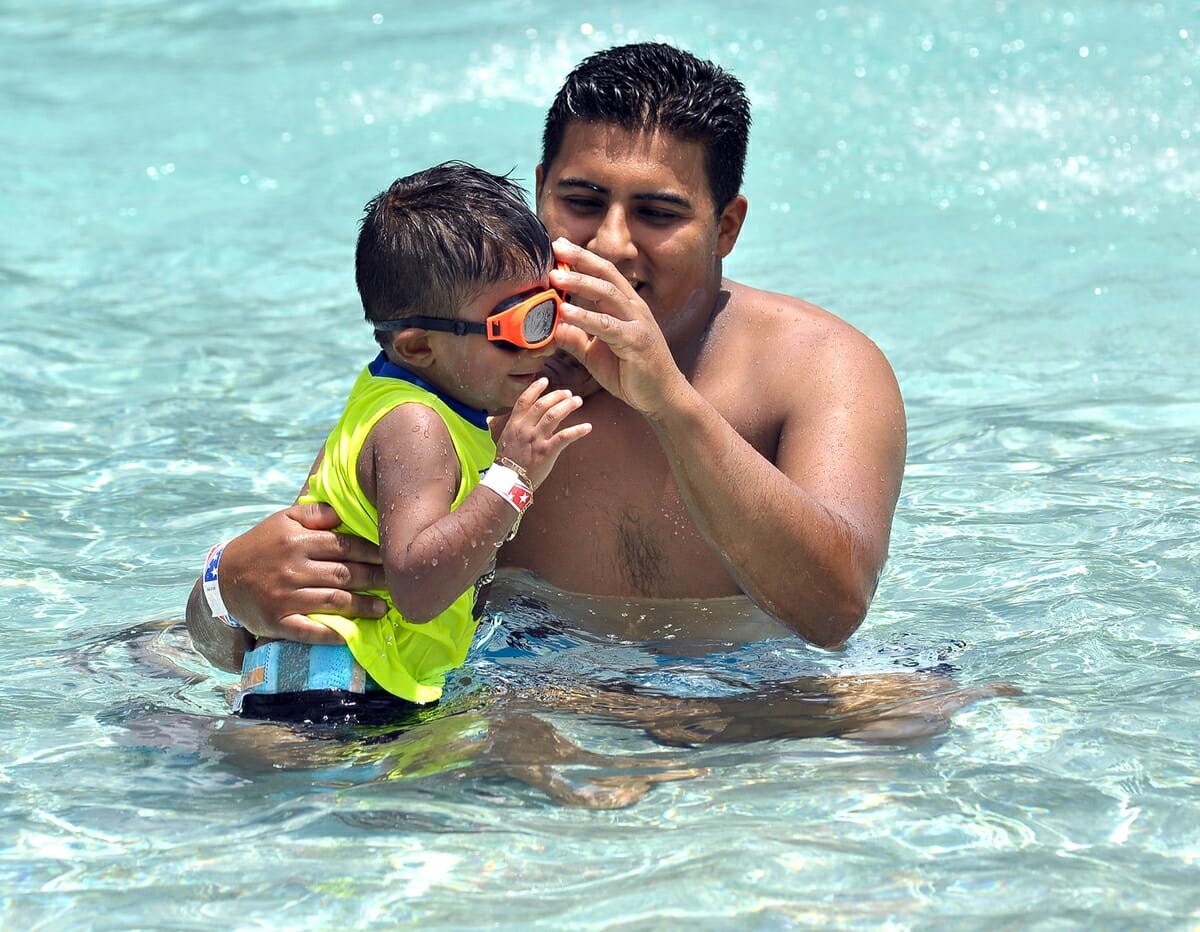 Jonathan Salazar makes sure his son Jothan’s goggles are adjusted properly while playing at the Green Street pool on the Fourth of July at Charles Lind Brown Center.