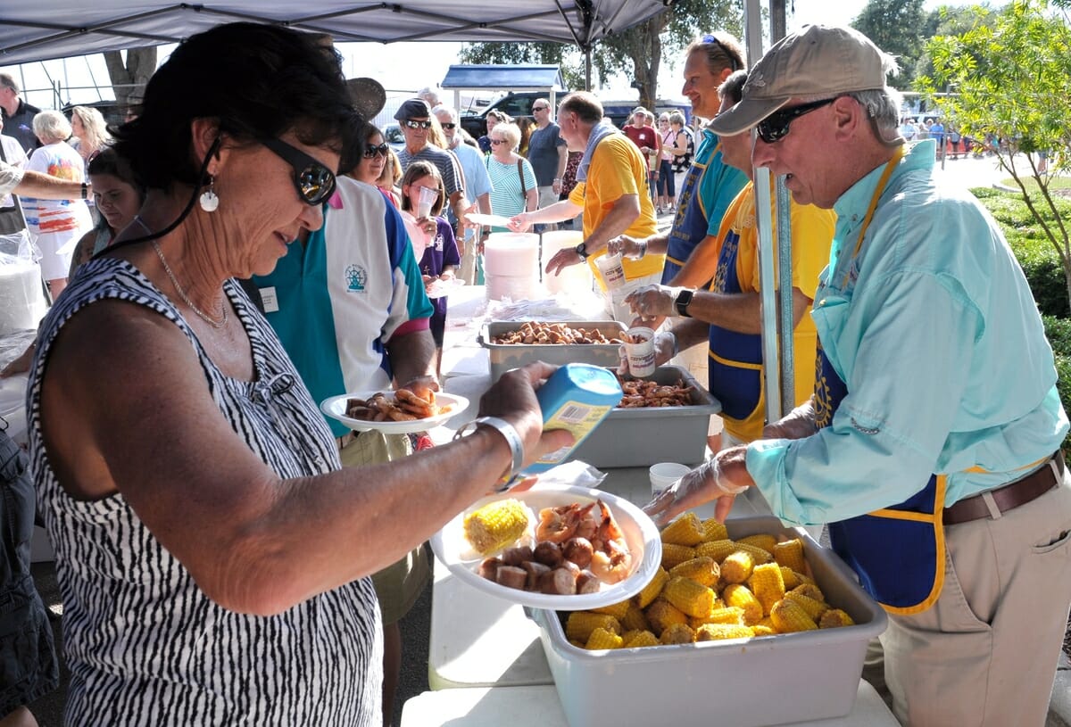 Marge Barber, left, squirts butter on her corn while volunteer Joe Lee, right, help her husband John during the annual Lowcountry Supper at Waterfront Park at the 2016 festival.