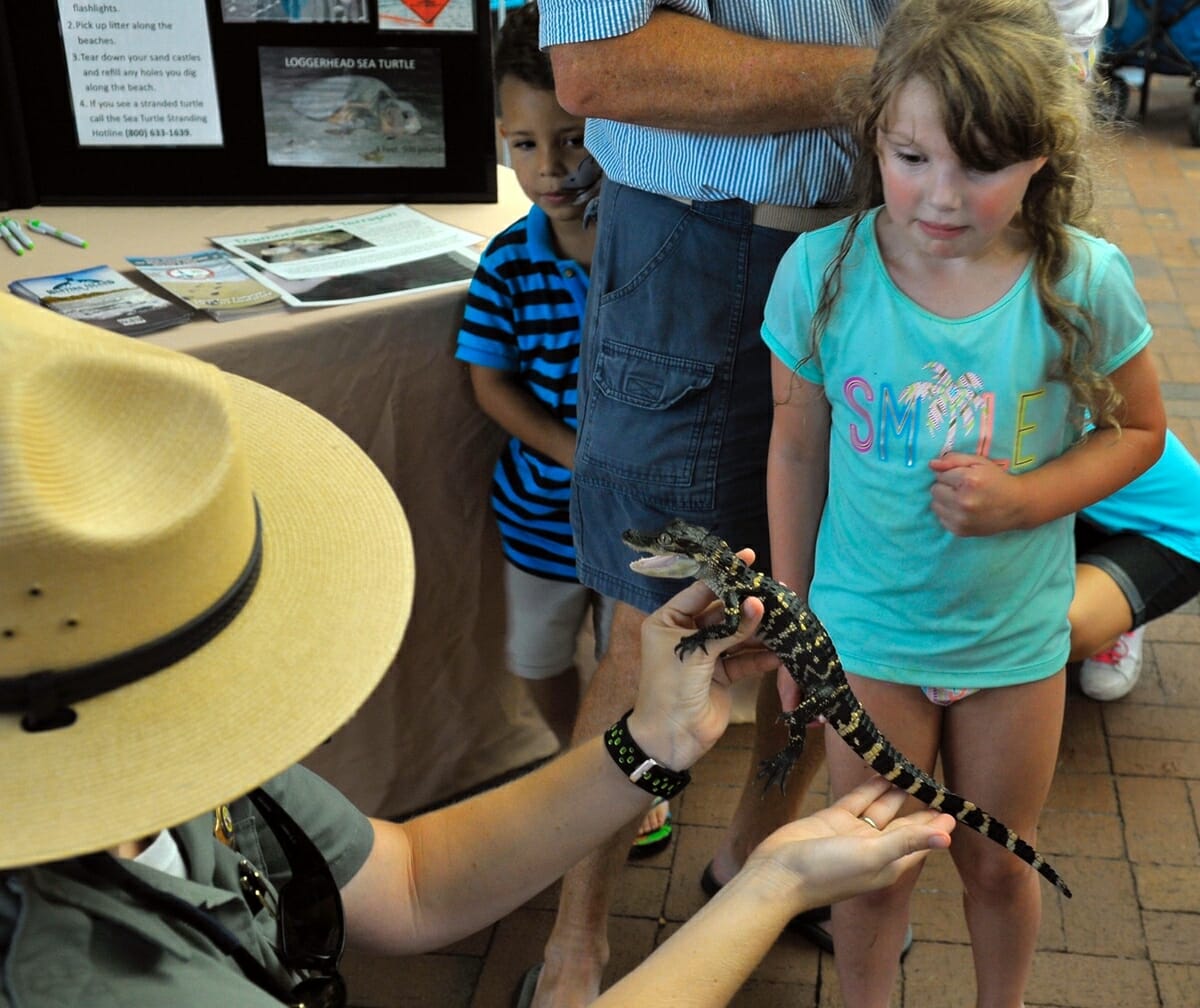 Ranger Megan Stegmeir, left, of Hunting Island State Park, holds a 3-year-old American alligator for children to touch on Children's Day at the Beaufort Water Festival. Stegmeir said the gator is small because captivity seems to stunt their growth. The child in the background was reluctant to even get close to it.