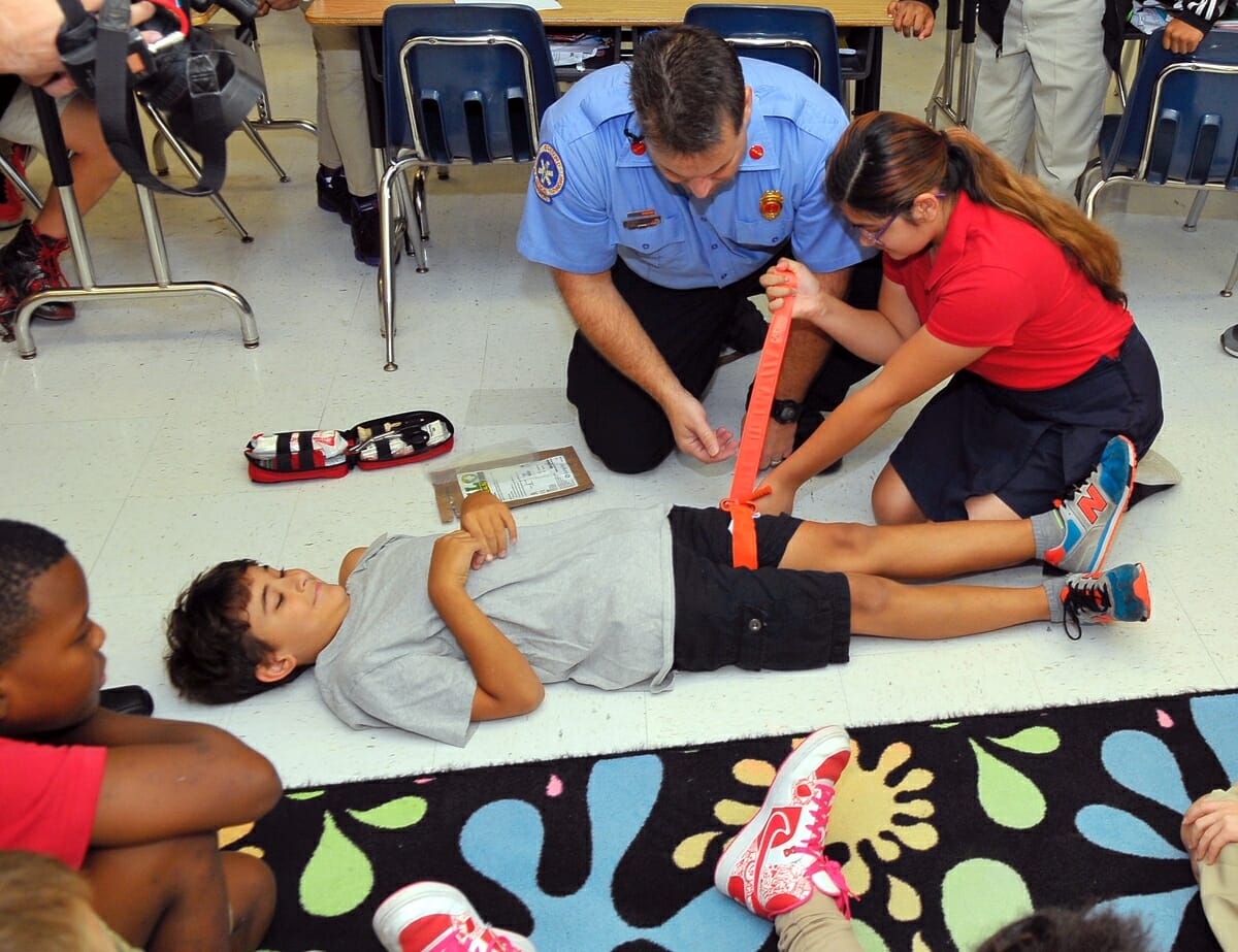 Hannah Boyd applies a tourniquet and locks it down with Velcro as Lt. Daniel Byrne of the Burton Fire District looks on. The demonstration at Port Royal Elementary School was intended to show the simplicity of using Jacob Kits. Photo by Bob Sofaly.