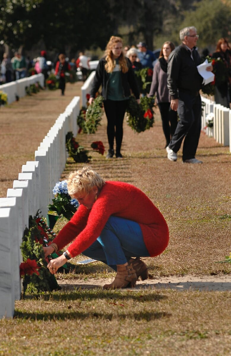 Janet Mulcahy adjust the wreathes at her parents’ headstones and displays an old black and white photo of her parents during Wreathes Across America at the Beaufort National Cemetery. Both her parents were U.S. Marine Corps veterans.